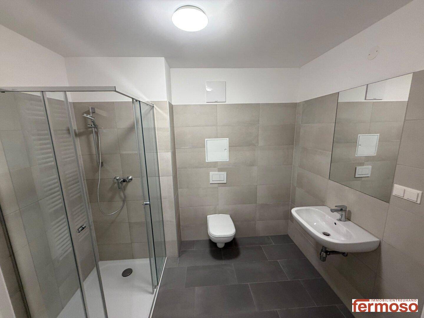 Modernes Badezimmer mit Duschkabine, Wand-WC, Einzelwaschbecken und hellen Fliesen.