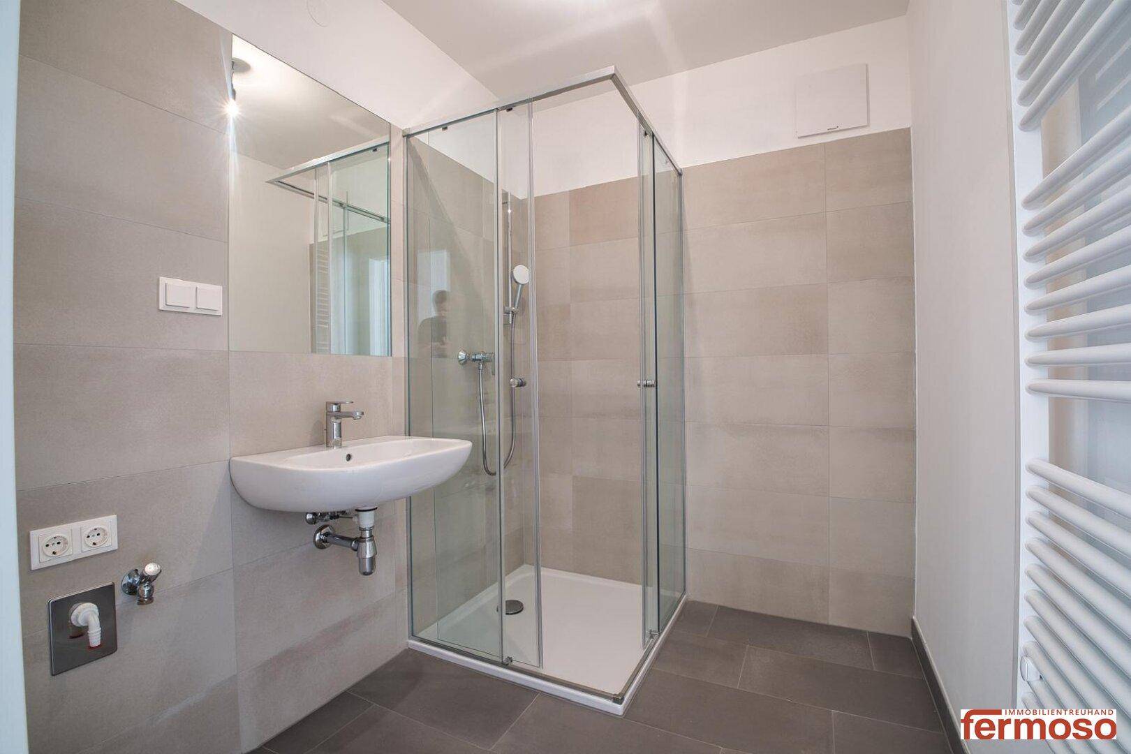 Modernes Badezimmer mit Duschkabine, Waschbecken und grauen Fliesen.