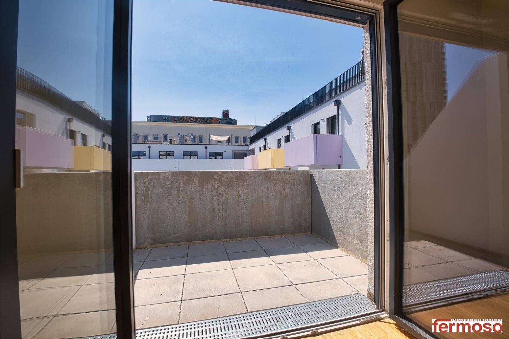 Blick vom Innenraum auf einen gefliesten Balkon mit Schiebetür und viel Tageslicht.