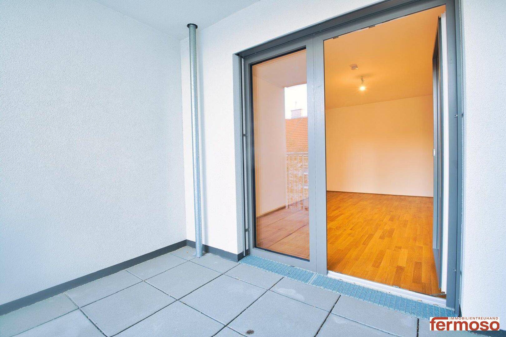 Leerer Balkon mit Fliesenboden und Blick auf die Umgebung.