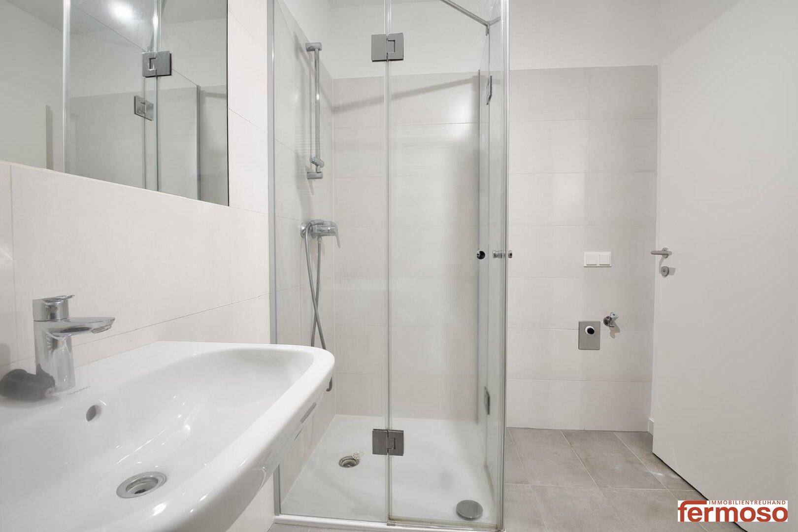 Modernes Badezimmer mit Duschkabine, Waschbecken und hellen Fliesen.