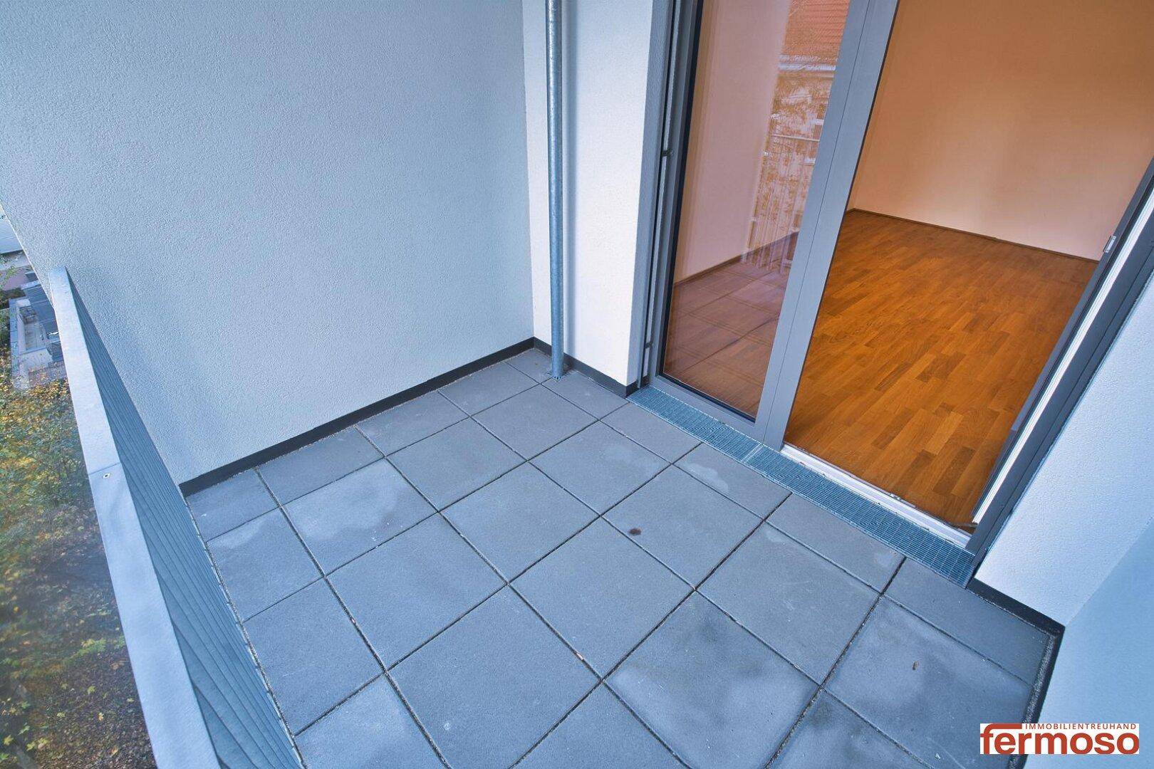 Heller Balkon mit Fliesenboden und Blick auf die Umgebung.