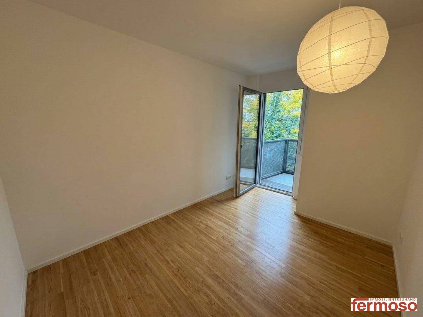 Leeres Schlafzimmer mit Parkettboden und Zugang zu einem Balkon.