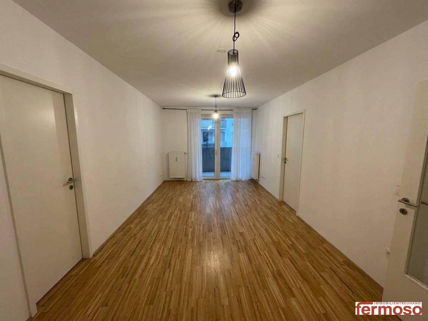 Langer, heller Raum mit Parkettboden und Zugang zu einem Außenbereich.