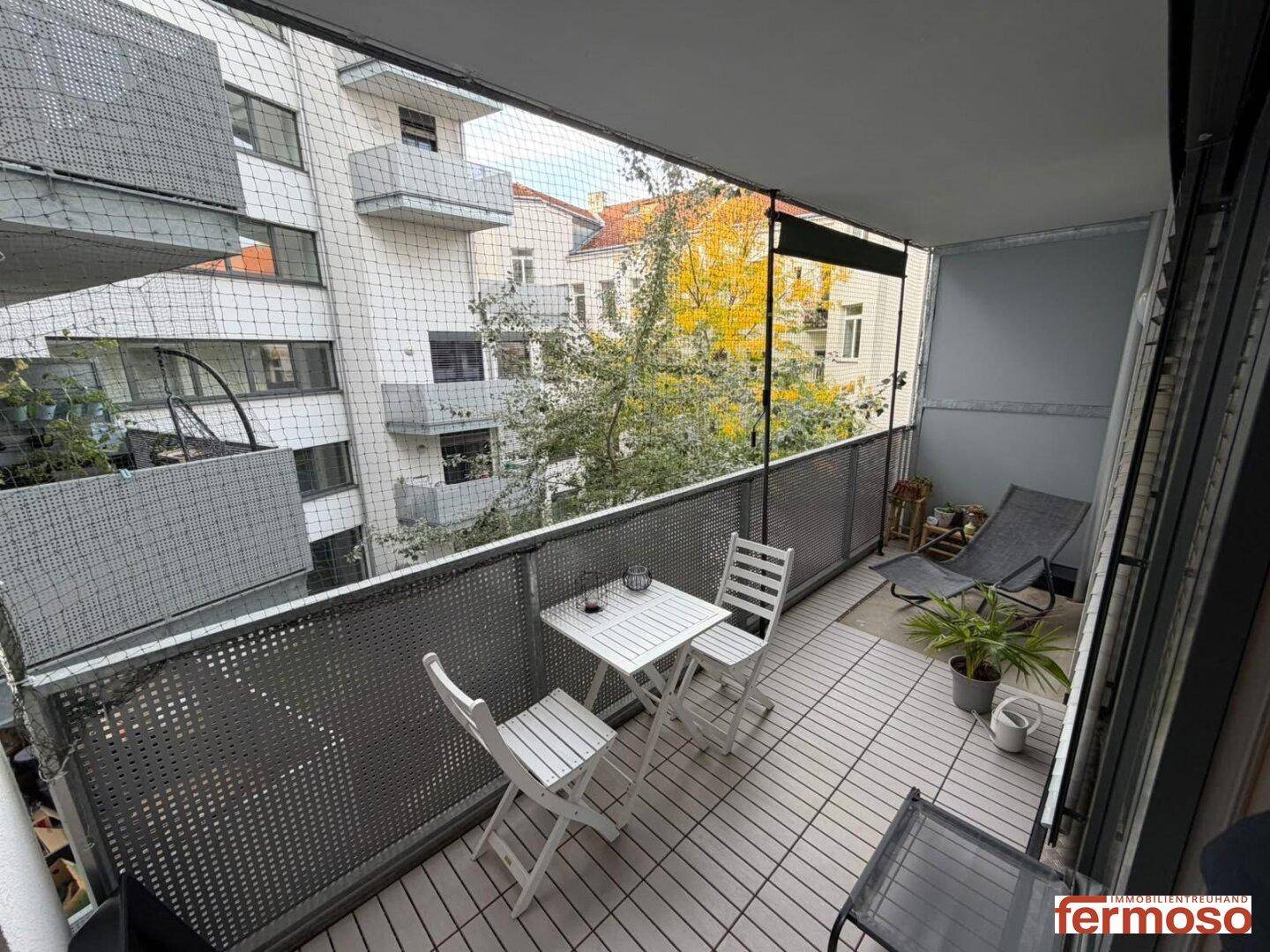 Möblierter Balkon mit Sitzgelegenheiten und Blick auf die umliegenden Gebäude und Bäume.