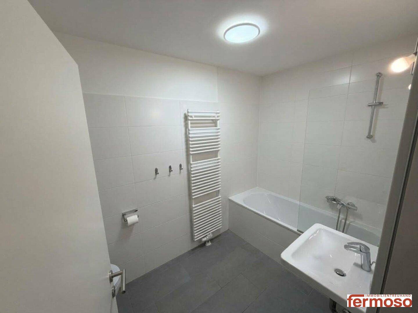 Helles Badezimmer mit Badewanne, Waschbecken, WC und beheiztem Handtuchhalter.