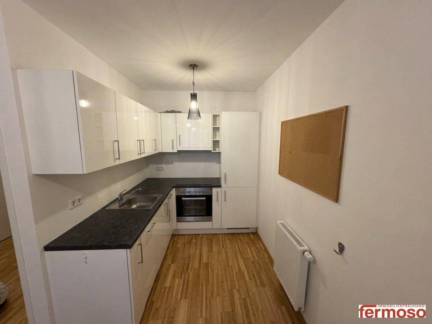 Moderne Küche mit weißen Hochglanzschränken, dunkler Arbeitsplatte und integriertem Ofen.