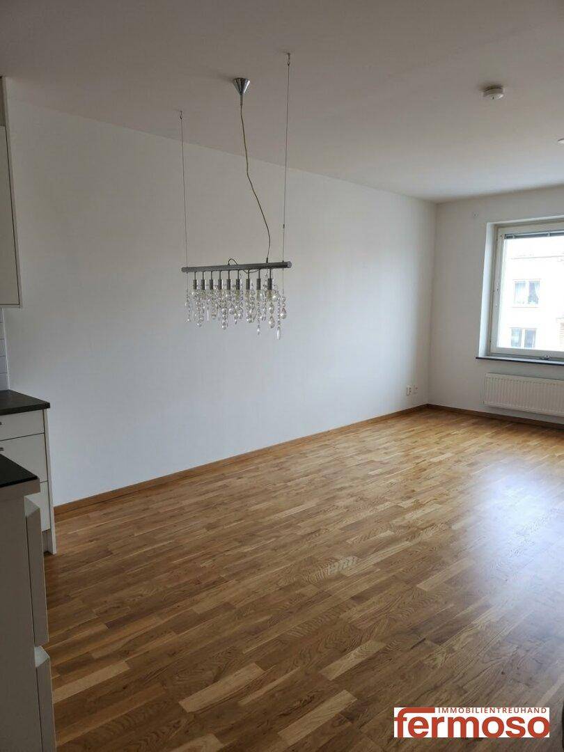 Geräumiger, leerer Wohn- und Essbereich mit hellem Holzboden und großem Fenster.