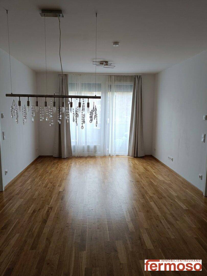 Heller Wohnbereich mit Holzboden und großer Glasfront, die viel Tageslicht hereinlässt.