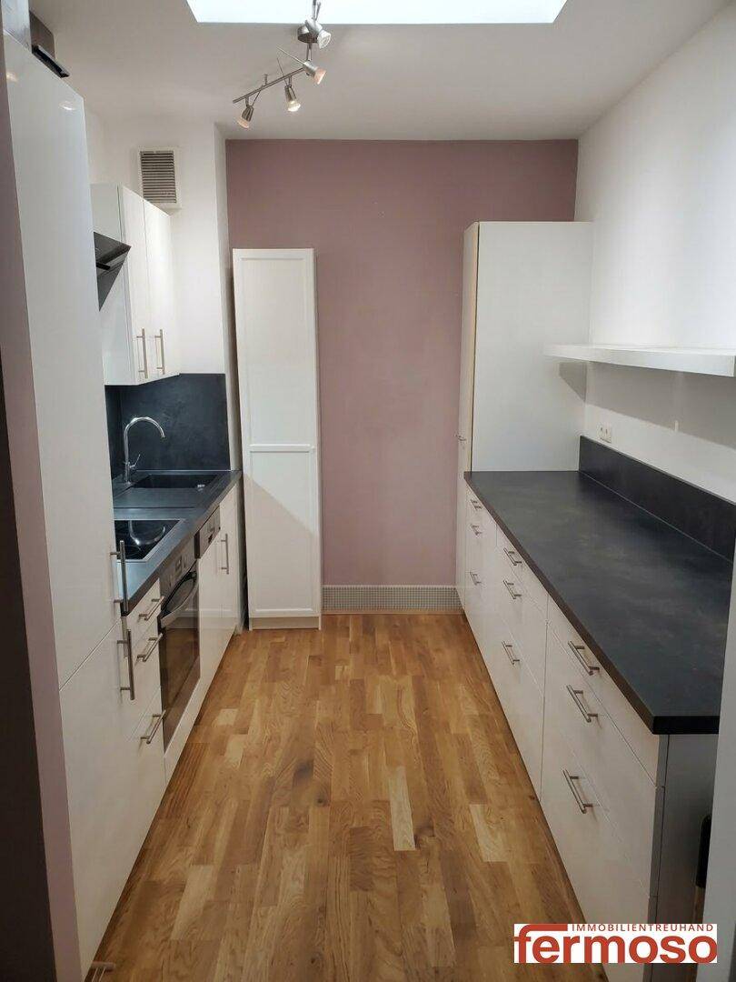 Schmale, funktionale Küche mit weißen Schränken, dunkler Arbeitsplatte und Holzboden.