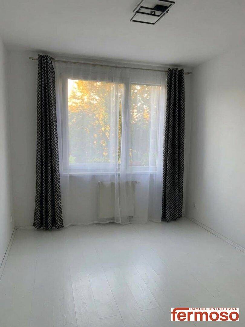 Helles Zimmer mit weißem Boden und großem Fenster, bereit zur individuellen Gestaltung.