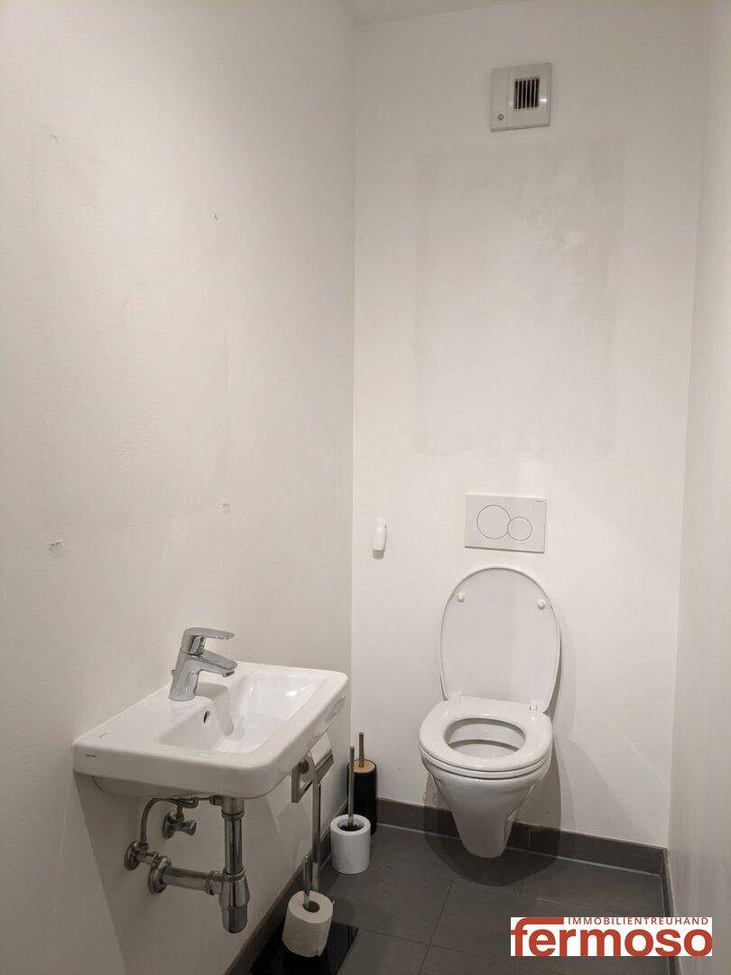 Kleines Gäste-WC mit Wand-WC, Waschbecken und dunklen Bodenfliesen.