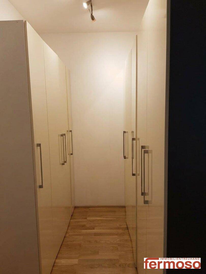 Langer Flur mit integrierten, glänzenden Schränken und Holzboden.