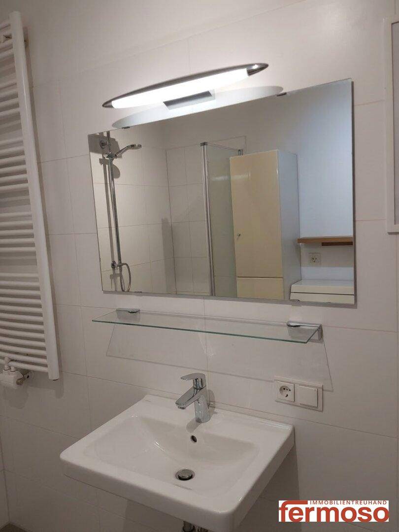 Helles Badezimmer mit Waschbecken, Spiegel und weiß gefliesten Wänden.
