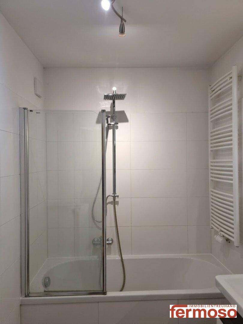 Badezimmer mit Badewanne, Duschabtrennung und weißer Fliesenverkleidung.