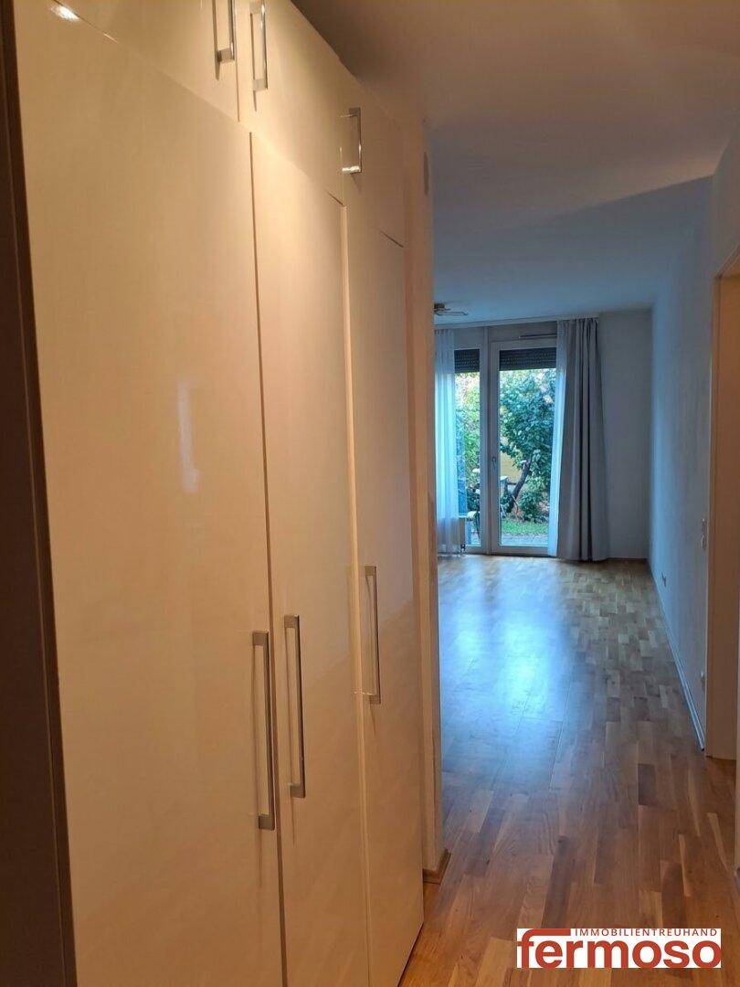 Heller Flur mit Holzboden, der zu einem Raum mit Zugang zum Außenbereich führt.