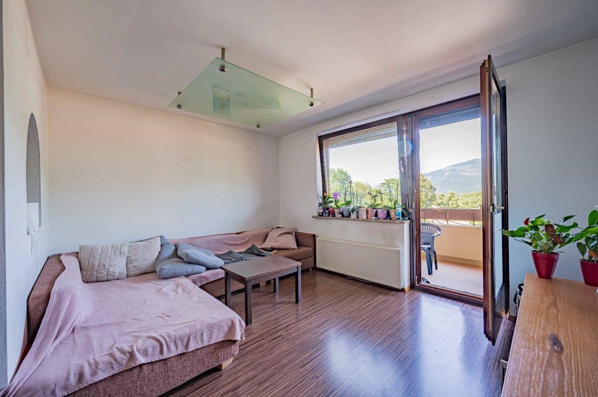 Helles Wohnzimmer mit Holzboden, bequemer Couch und Zugang zu einem Balkon mit Bergblick.