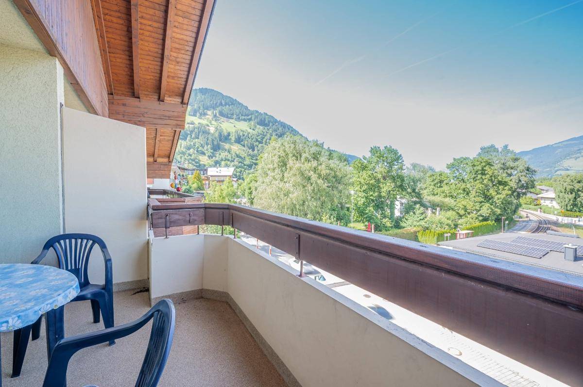 Sonniger Balkon mit Sitzgelegenheiten und weitem Blick auf grüne Berge und die Umgebung.