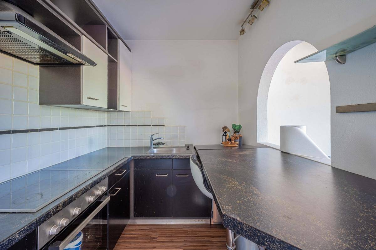 Funktionale Küche mit schwarzen Arbeitsplatten, weißen Fliesen und einem Durchgang zu einem anderen Bereich.