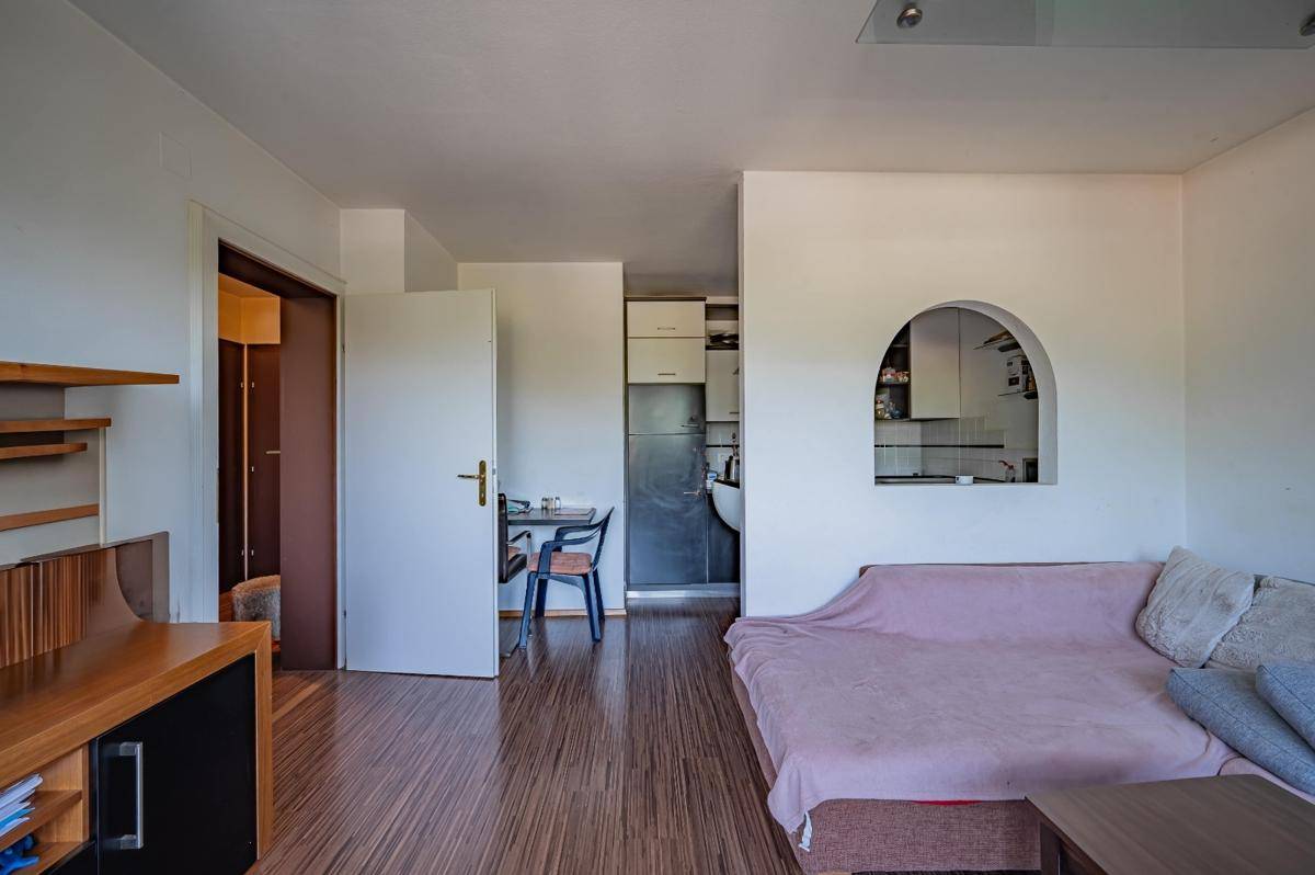 Wohnbereich mit Holzboden und einem Durchgang zu einem Essbereich oder einer kleinen Küche.