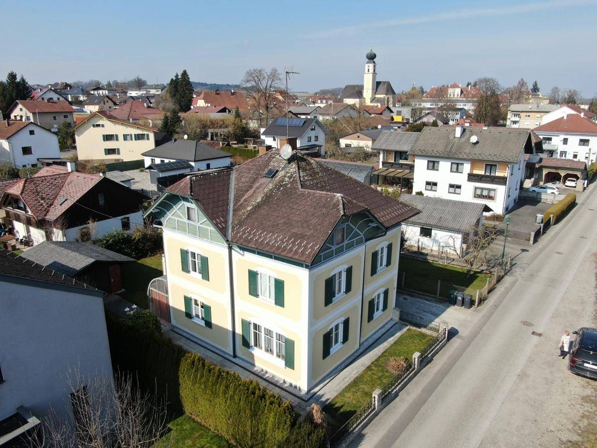 Luftaufnahme des Wohnhauses in einer ländlichen Umgebung mit Blick auf die Kirchturmspitze.