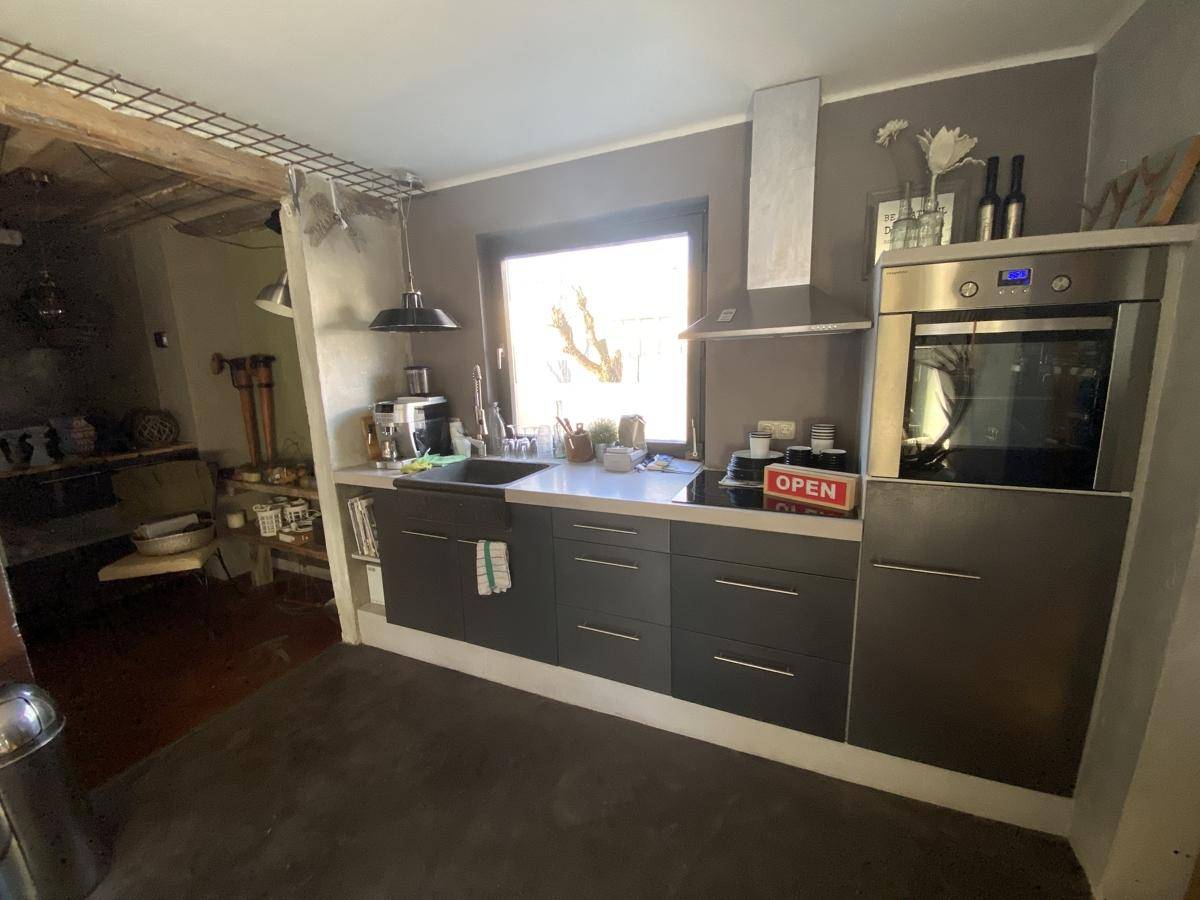 Moderne Küche mit dunklen Schränken, integriertem Backofen, Induktionskochfeld und Fenster.