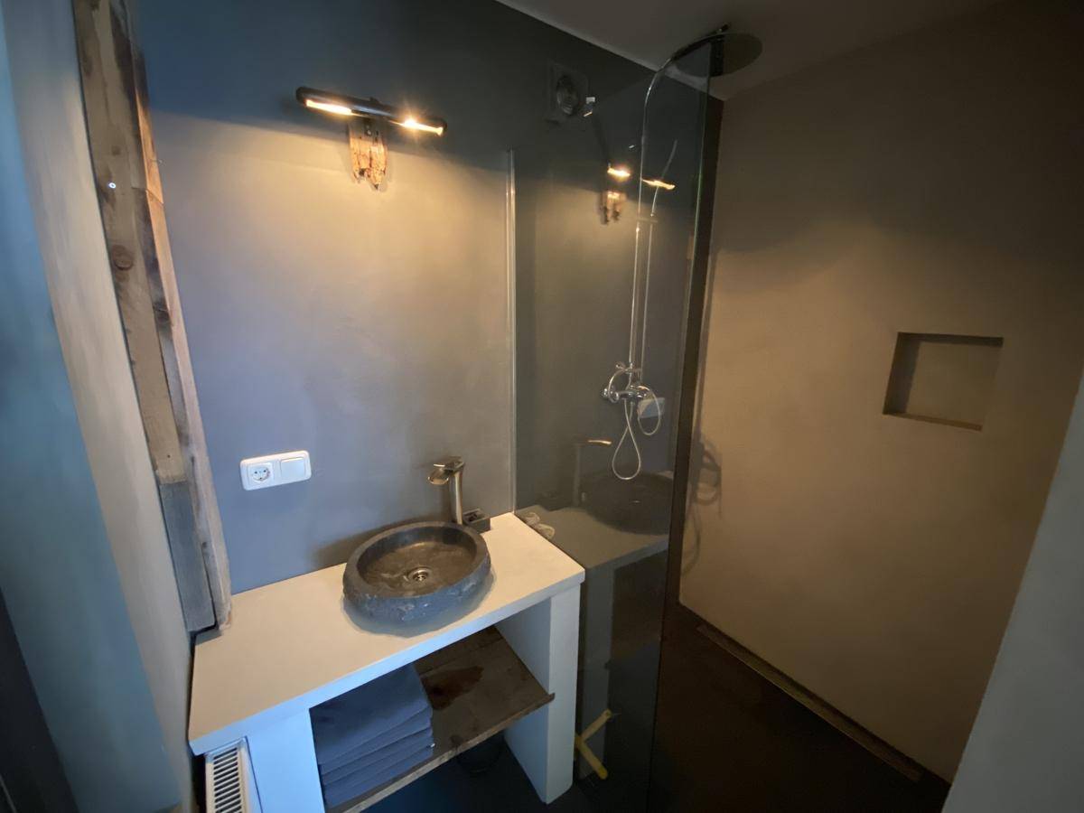 Modernes Badezimmer mit begehbarer Dusche, einzigartigem Steinwaschbecken und minimalistischem Design.