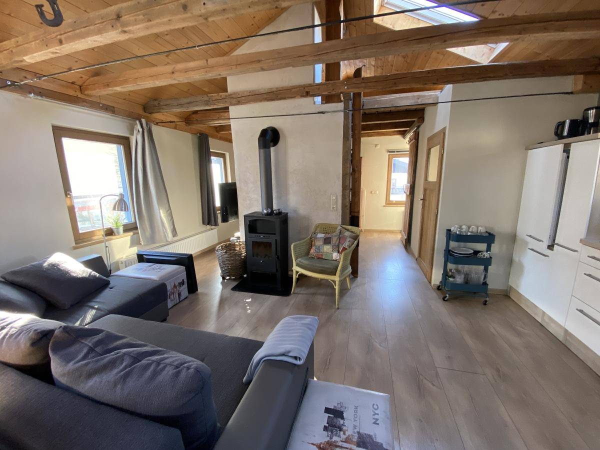 Helles Wohnzimmer im Obergeschoss mit Holzbalkendecke, Kaminofen und Laminatboden.