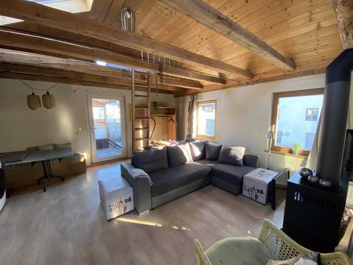 Geräumiges Wohnzimmer mit Kaminofen, Holzbalkendecke und direktem Zugang zur Terrasse.
