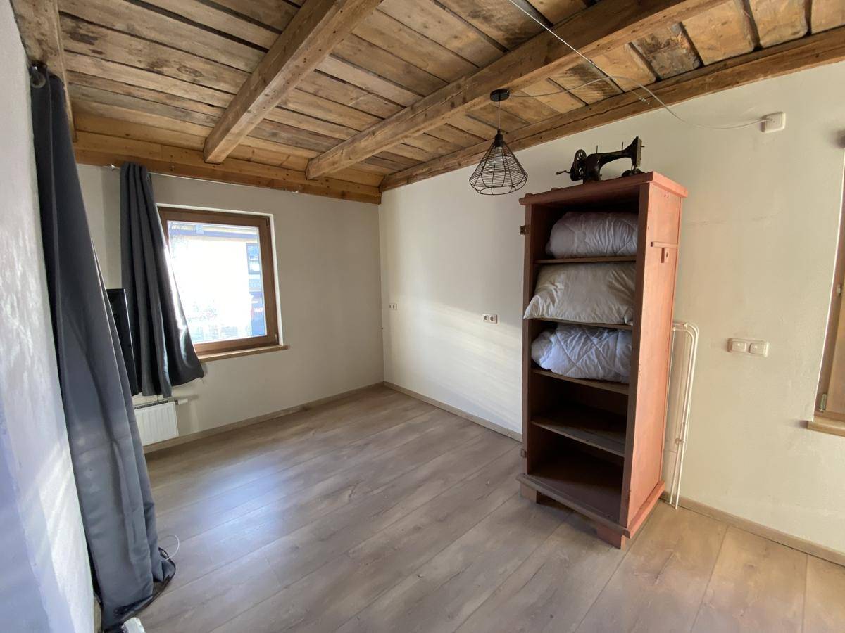 Schlafzimmer mit Holzbalkendecke, Laminatboden und natürlichem Lichteinfall durch das Fenster.