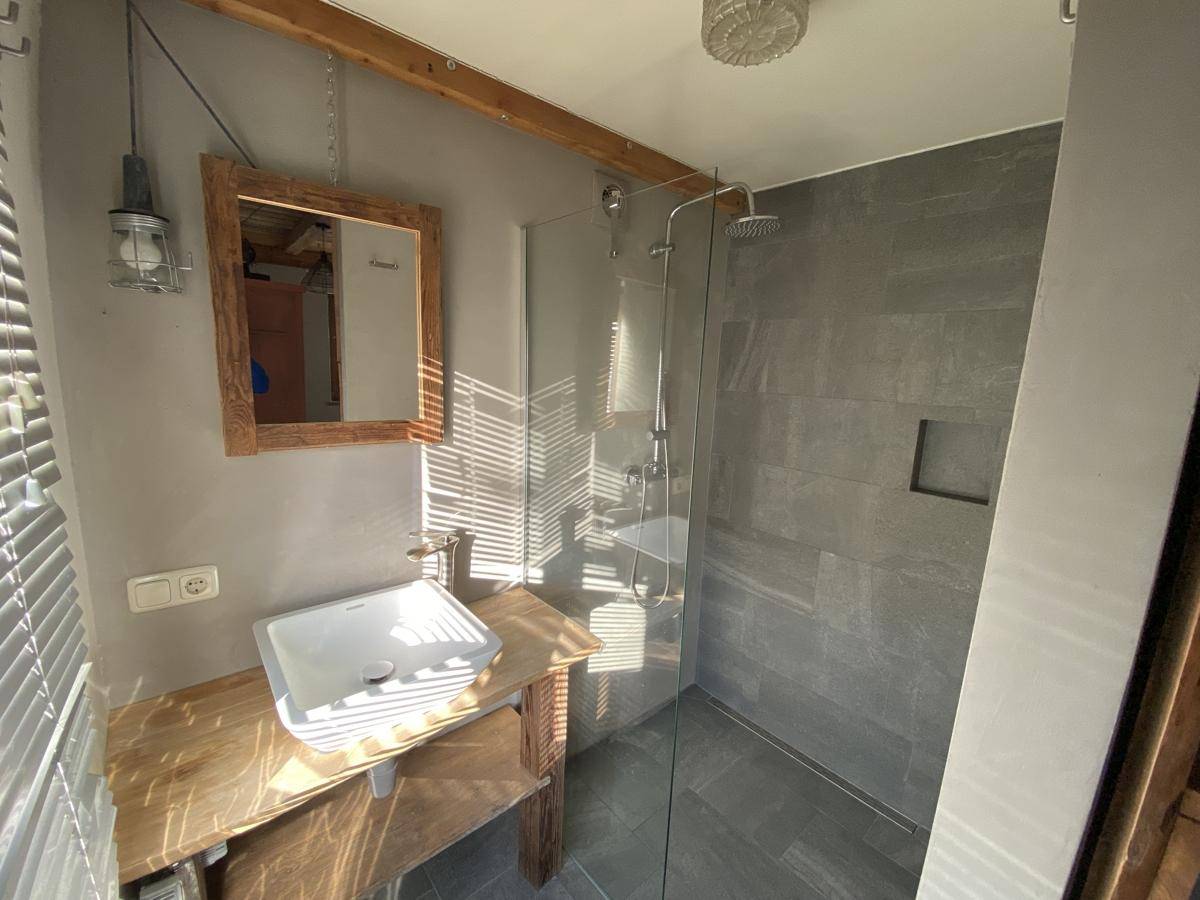Modernes Badezimmer mit grauen Fliesen, begehbarer Dusche und Holzwaschtisch mit Aufsatzbecken.