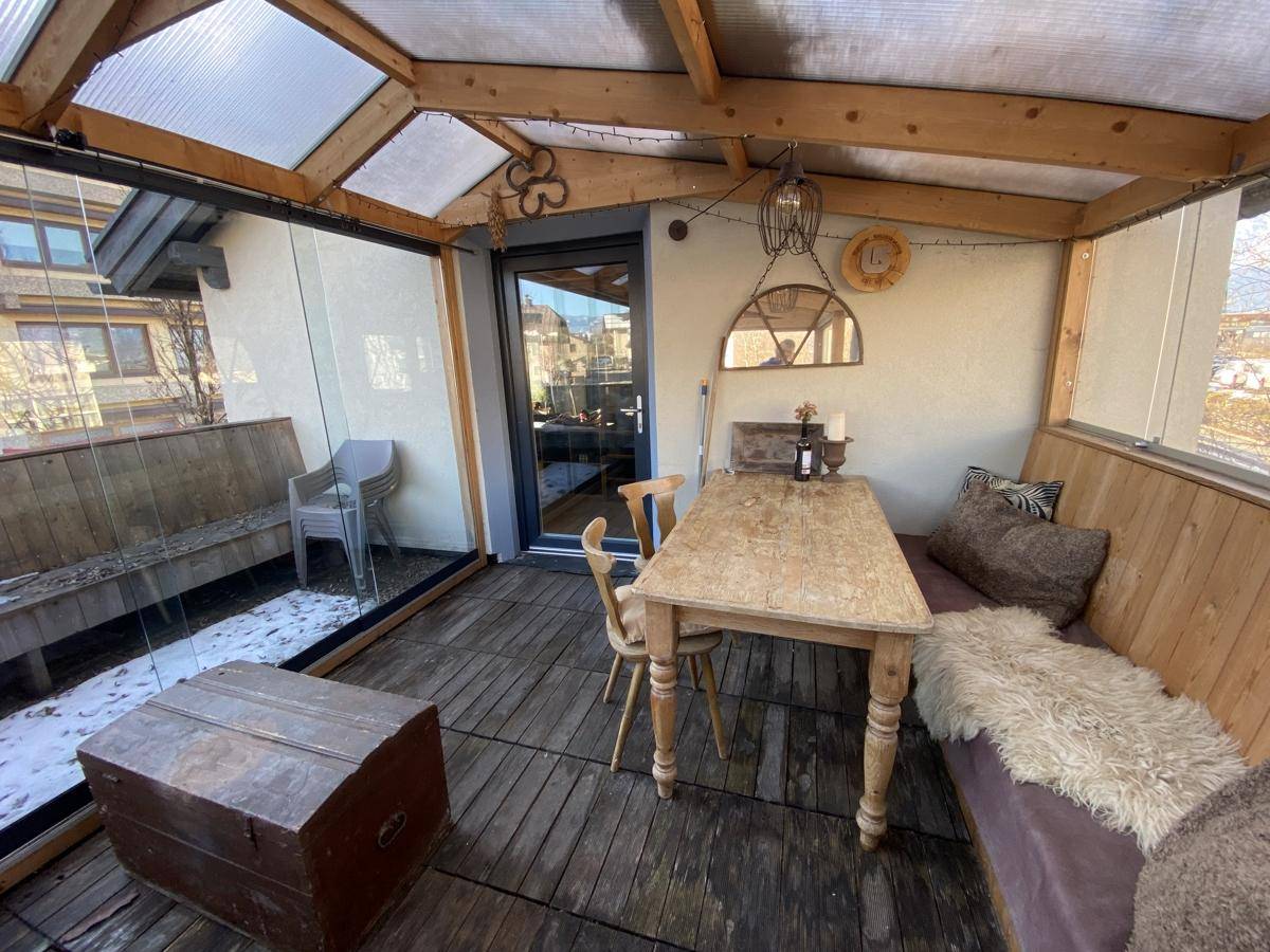 Gemütlicher Wintergarten mit Holzboden, Sitzgelegenheiten und viel Tageslicht, ideal zum Entspannen.