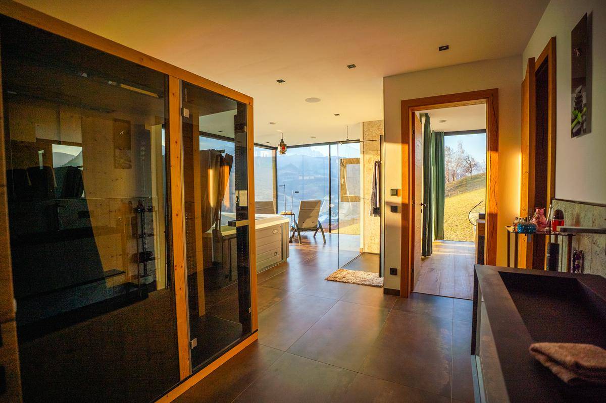 Luxuriöse Wellnessoase mit Sauna, Whirlpool und atemberaubendem Bergblick durch große Glasfronten.