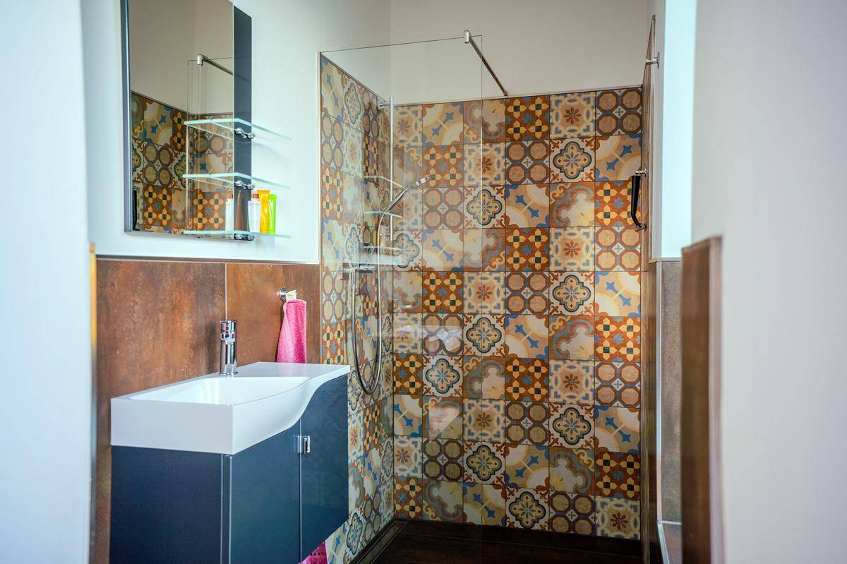 Badezimmer mit farbenfrohen, gemusterten Fliesen, modernem Waschbecken und einer Duschkabine.