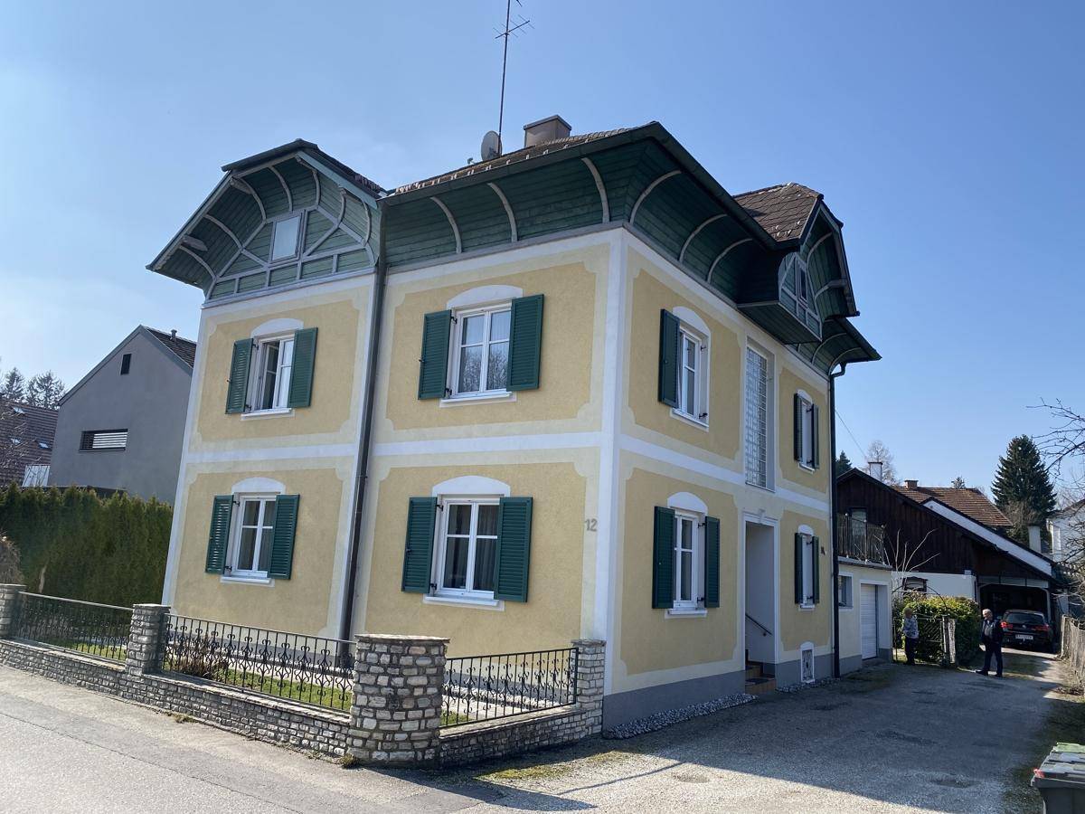 Charmantes gelbes Haus mit grünen Fensterläden und gepflegtem Vorgarten an sonnigem Tag.