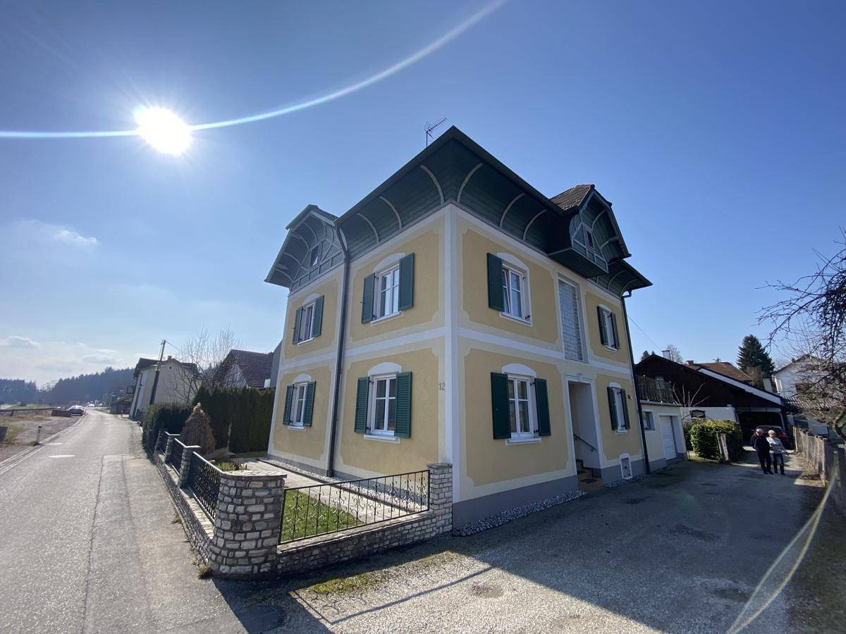 Sonniges gelbes Haus mit grünen Fensterläden und gepflegter Auffahrt in ländlicher Umgebung.
