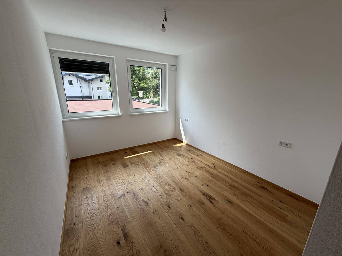 Schlafzimmer mit hellem Parkettboden und zwei Fenstern für viel Tageslicht.