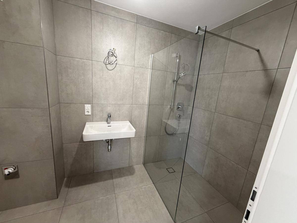 Modernes Badezimmer mit großformatigen Fliesen, ebenerdiger Dusche und Einzelwaschbecken.