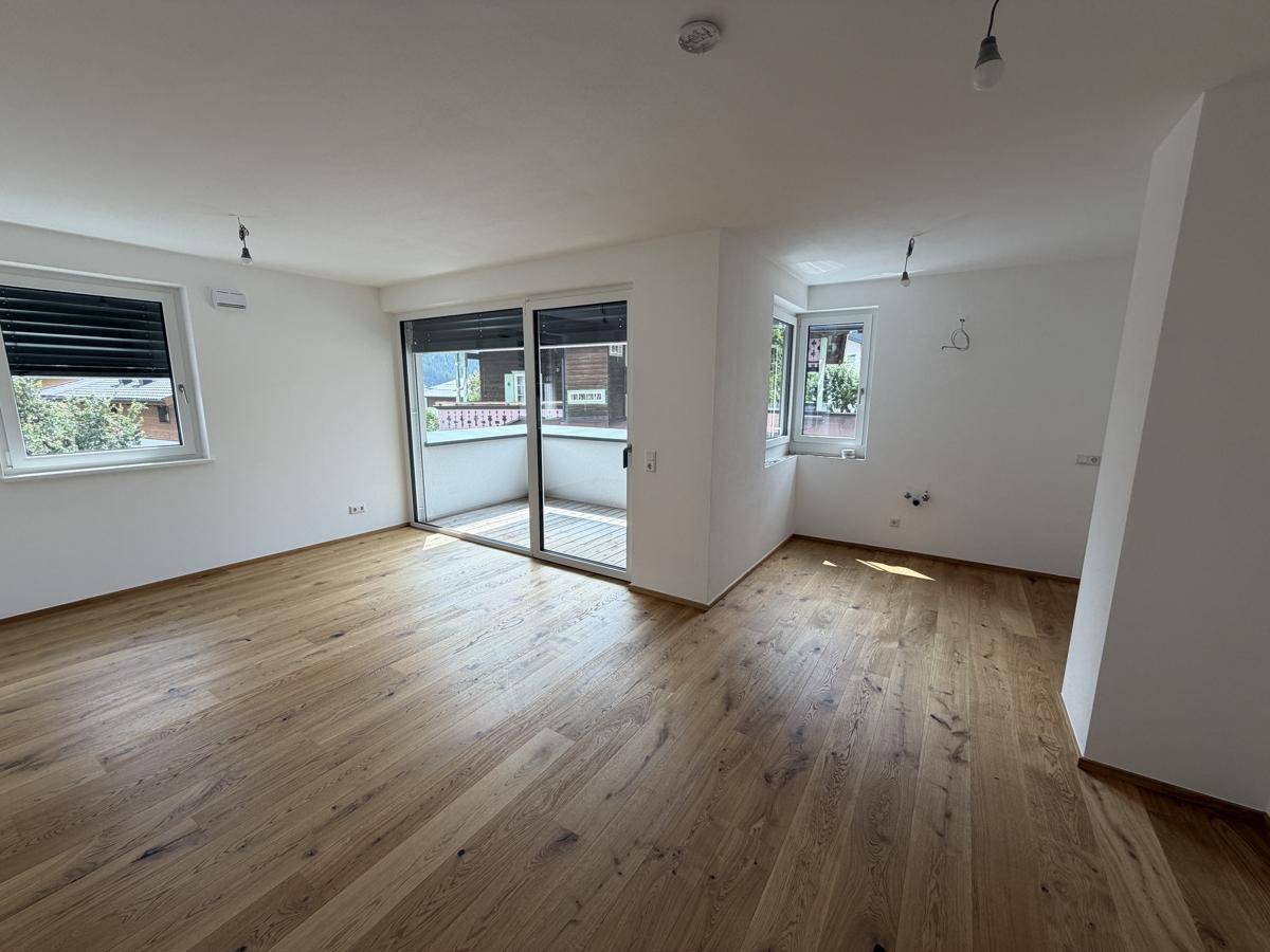 Heller Wohnraum mit neuem Parkettboden und Zugang zu einem Balkon.