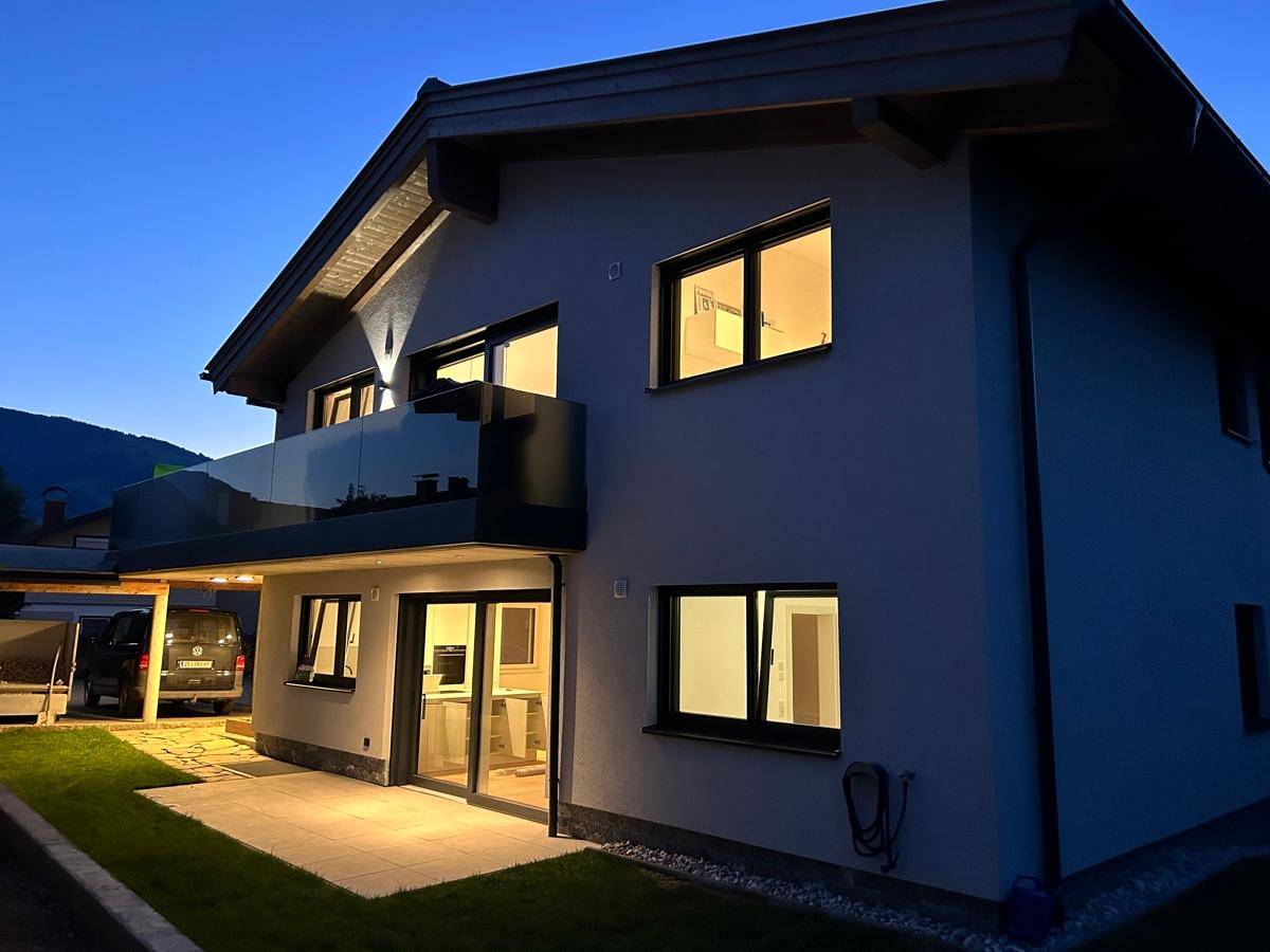 Modernes Einfamilienhaus bei Dämmerung mit beleuchteten Innenräumen und Balkon.