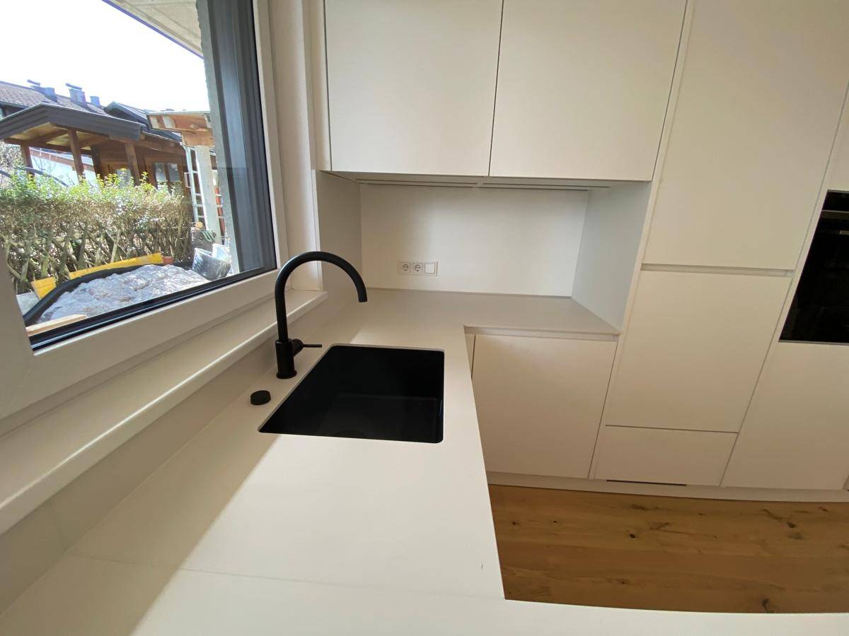Moderner Küchenbereich mit schwarzem Wasserhahn, weißer Arbeitsplatte und Fensterblick.
