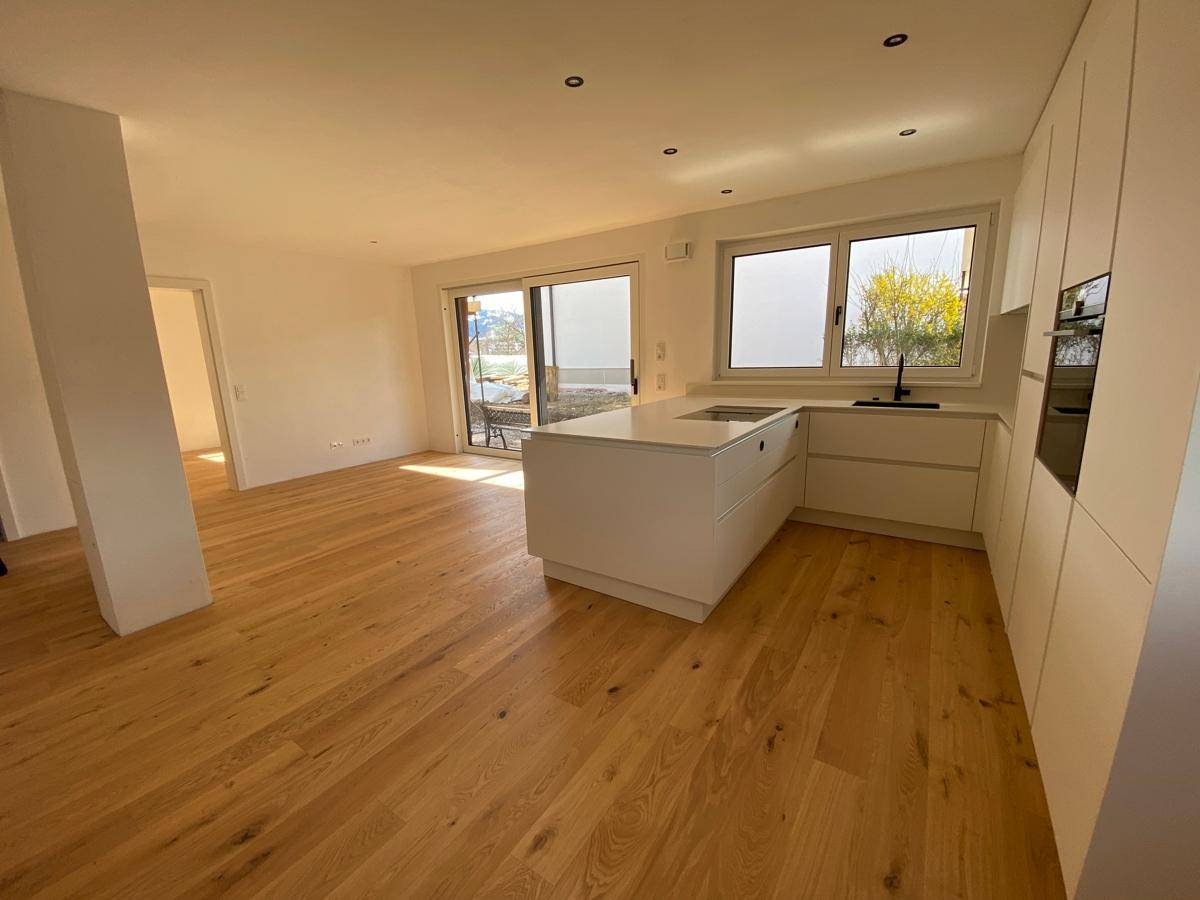 Offener Wohnbereich mit moderner Küche, Holzboden und großem Schiebetürzugang zur Terrasse.