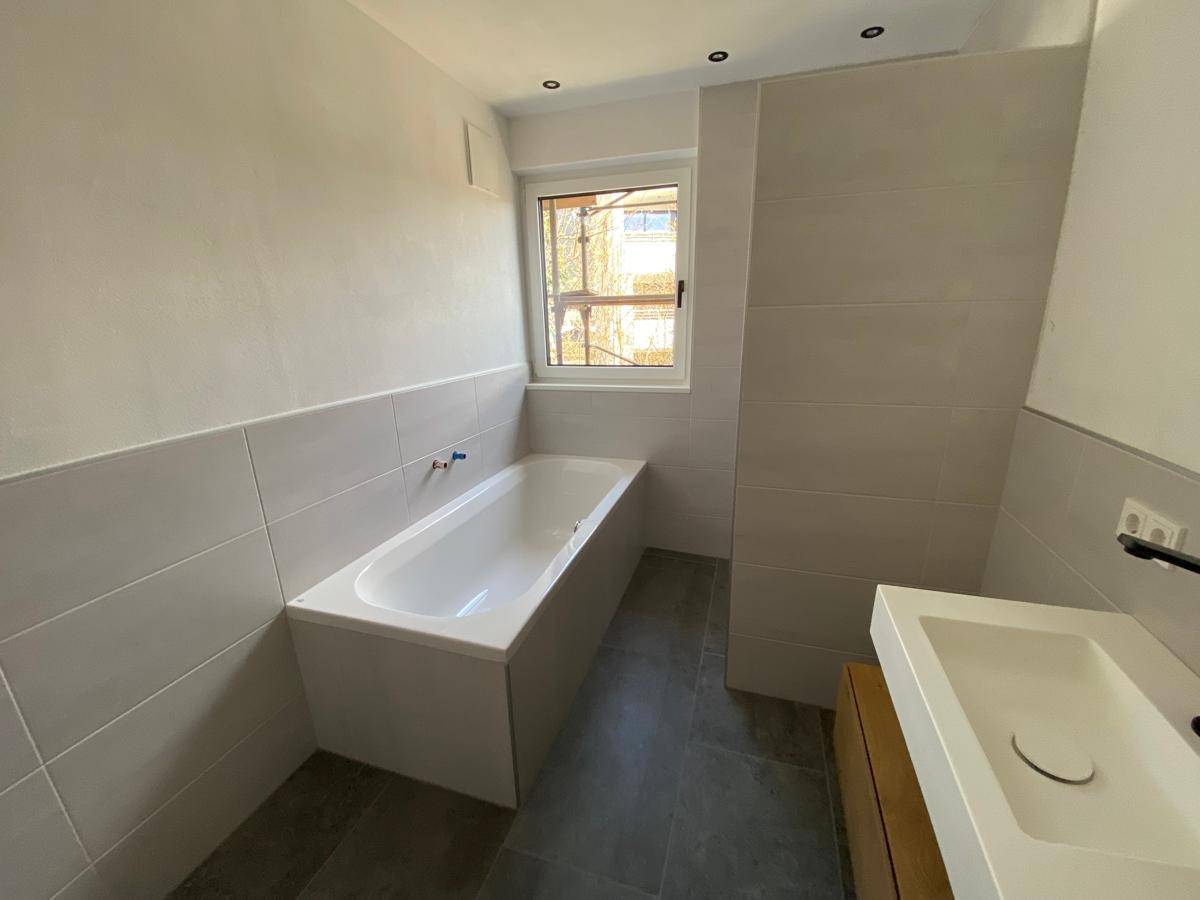Modernes Badezimmer mit Badewanne, Einzelwaschbecken, grauen Fliesen und Fenster.