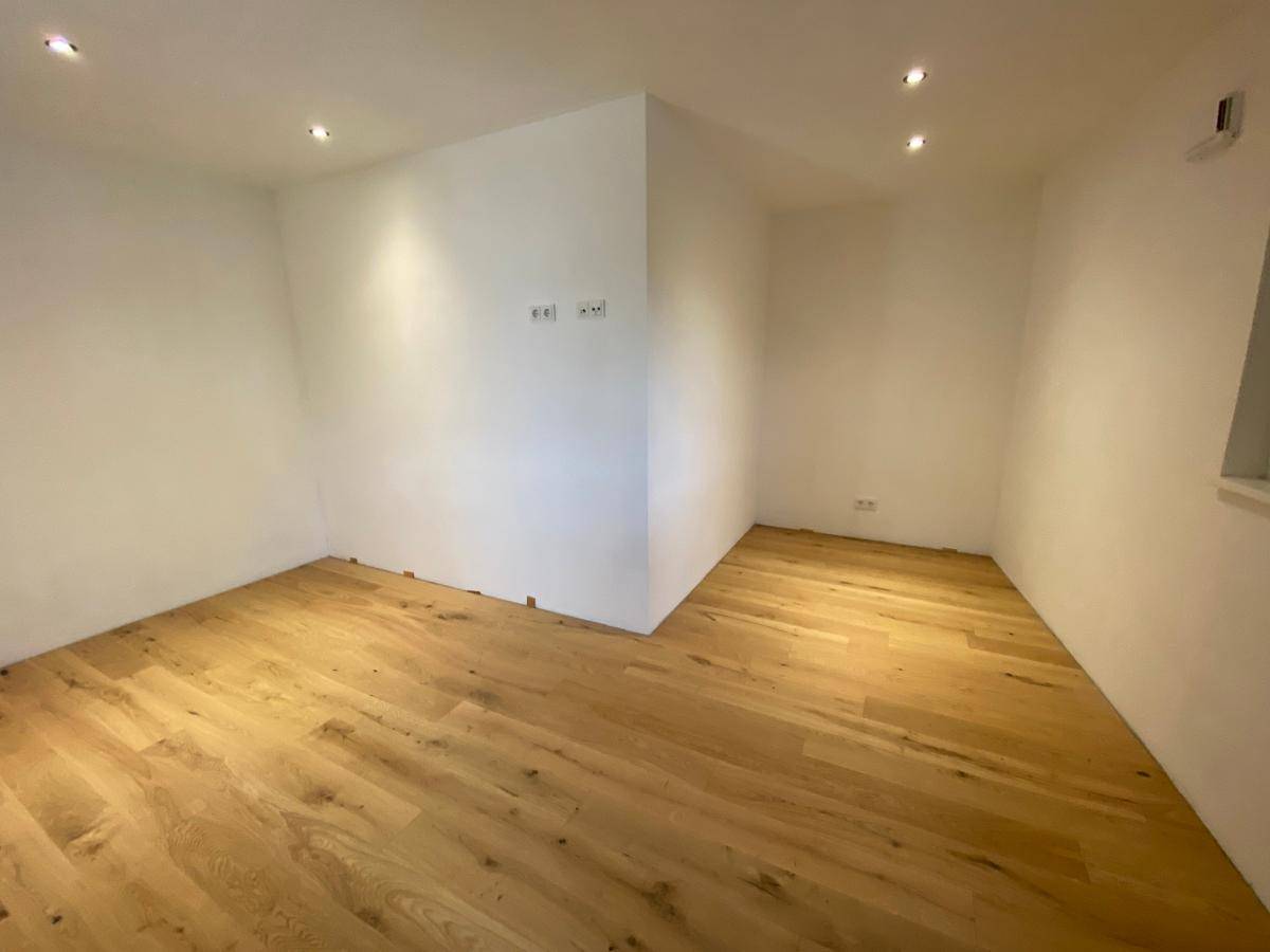 Helles Zimmer mit Holzboden und weißen Wänden, ausgestattet mit moderner Deckenbeleuchtung.