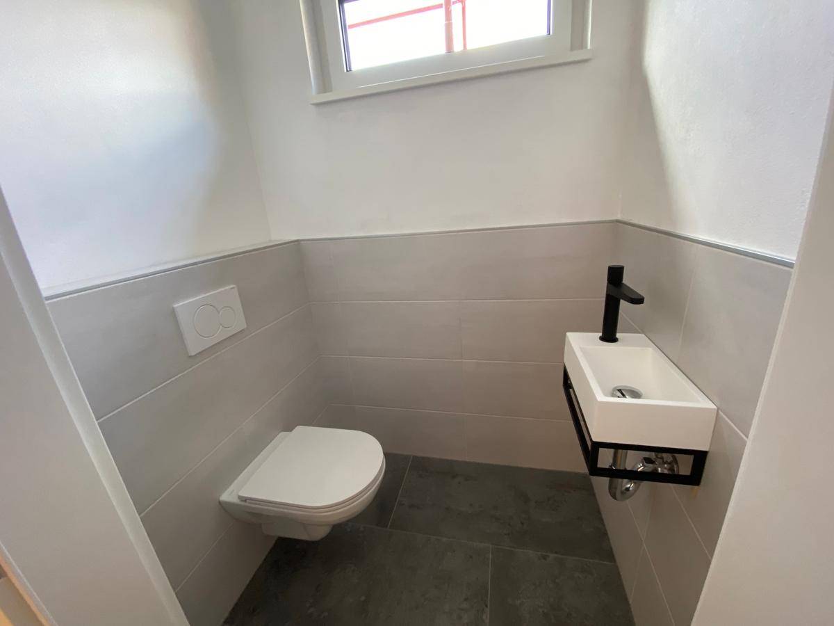 Modernes Gäste-WC mit Wand-WC und kleinem Waschbecken, in neutralen Farbtönen gehalten.