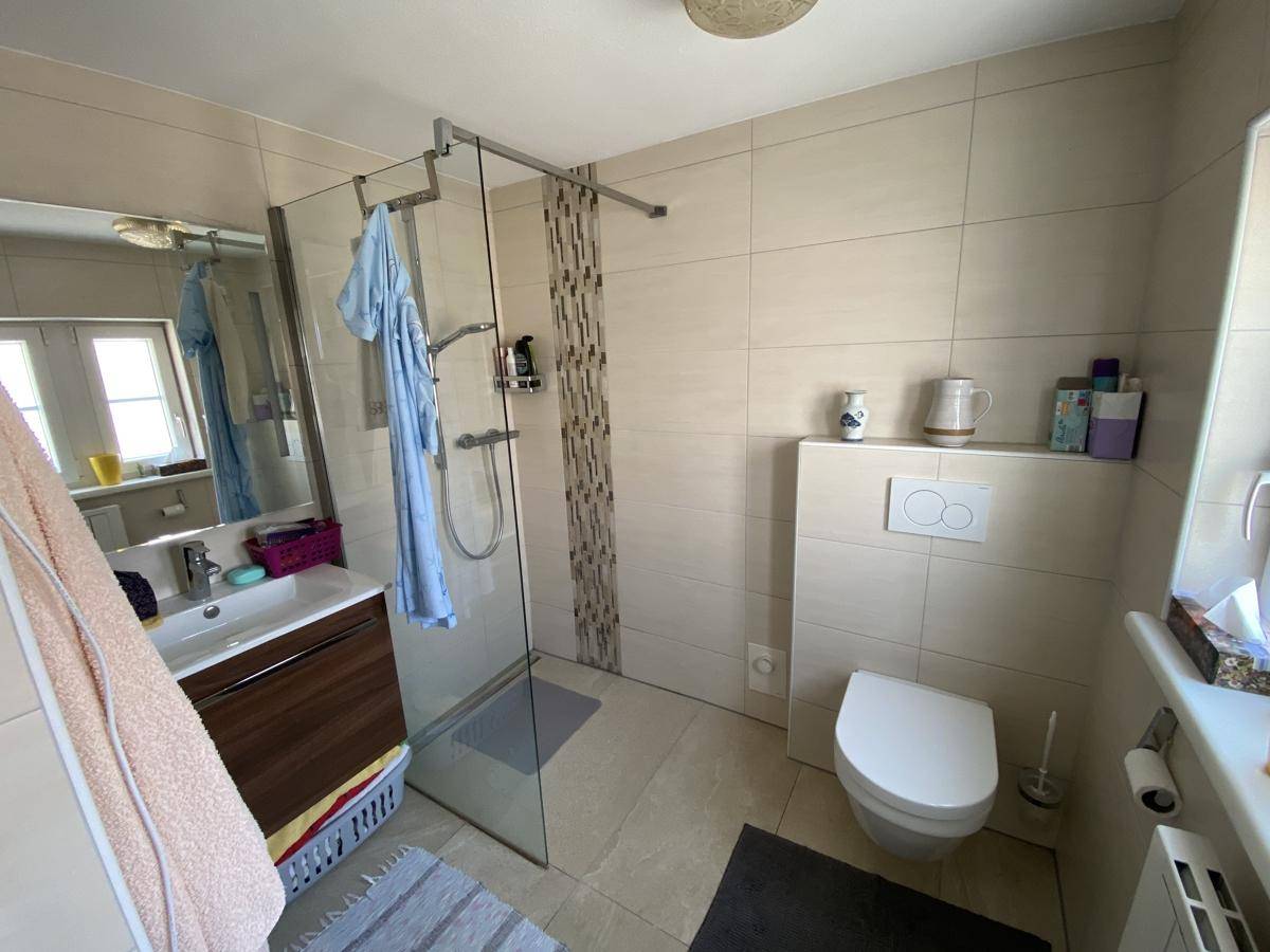 Modernes Badezimmer mit begehbarer Dusche, wandhängendem WC und beigefarbenen Fliesen.