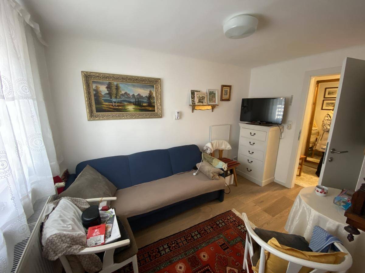 Helles Wohnzimmer mit Sofa, Fernseher und traditionellem Teppichboden.