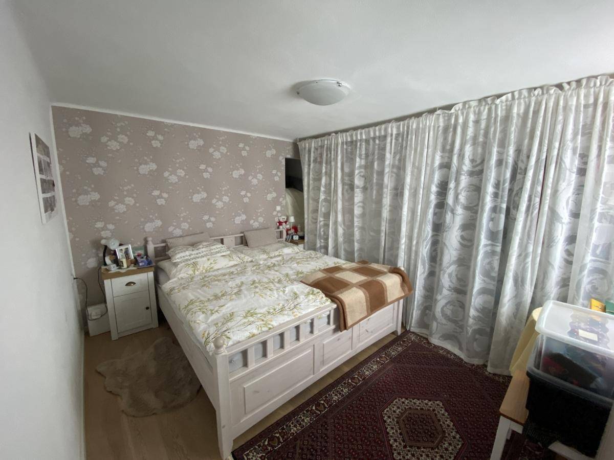 Gemütliches Schlafzimmer mit Doppelbett, floraler Tapete und Vorhängen vor dem Fenster.