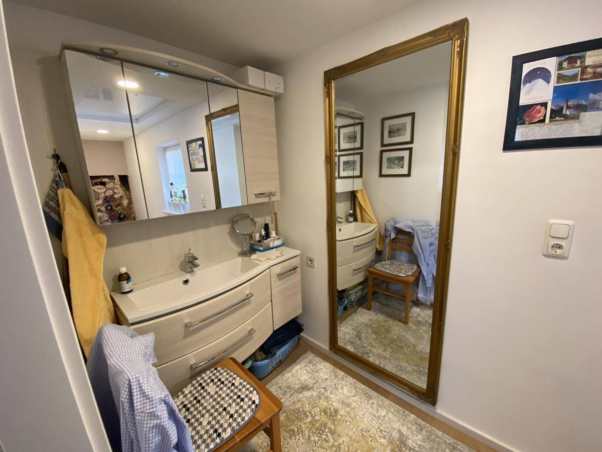 Badezimmer mit Waschbecken, Spiegelschrank und großem Wandspiegel in Goldrahmen.