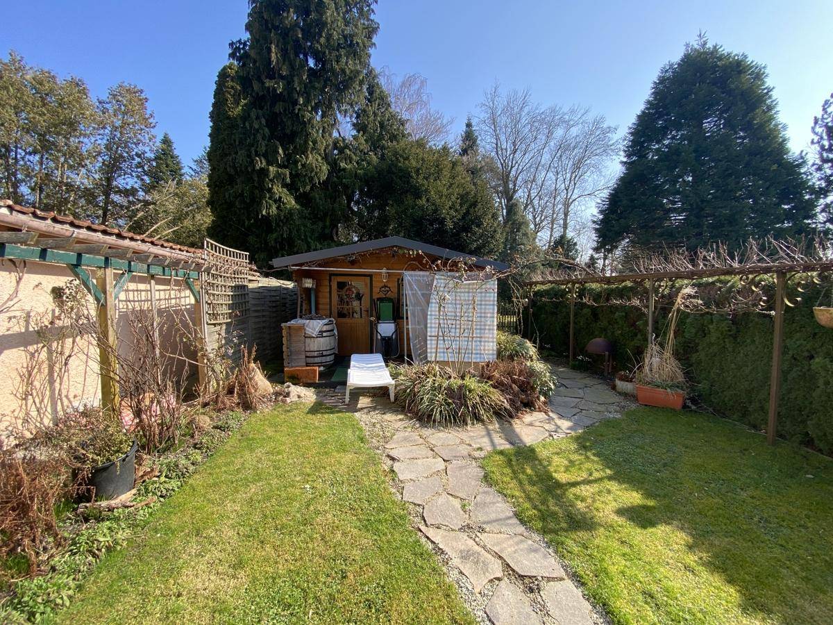 Gepflegter Garten mit Gartenhaus, Rasenfläche und Steinpfad unter blauem Himmel.